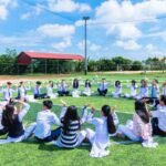 Students seated in a circle on a school field engaging in outdoor activities.