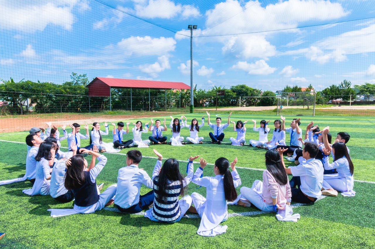 Students seated in a circle on a school field engaging in outdoor activities.