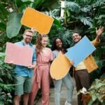 Cheerful group of friends holding colorful speech bubbles in a lush greenhouse setting.