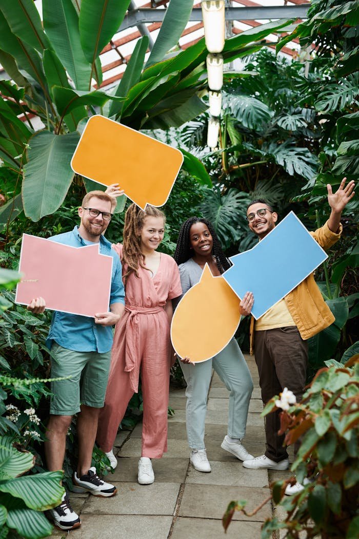 Cheerful group of friends holding colorful speech bubbles in a lush greenhouse setting.